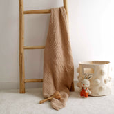 Latte 4-ply organic muslin baby blanket hanging beside wooden toy basket